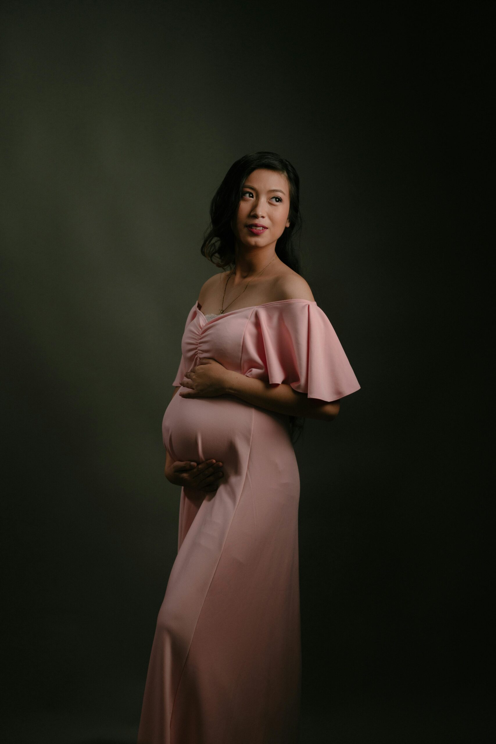 Beautiful portrait of a pregnant woman in a pink dress, captured in a studio setting.