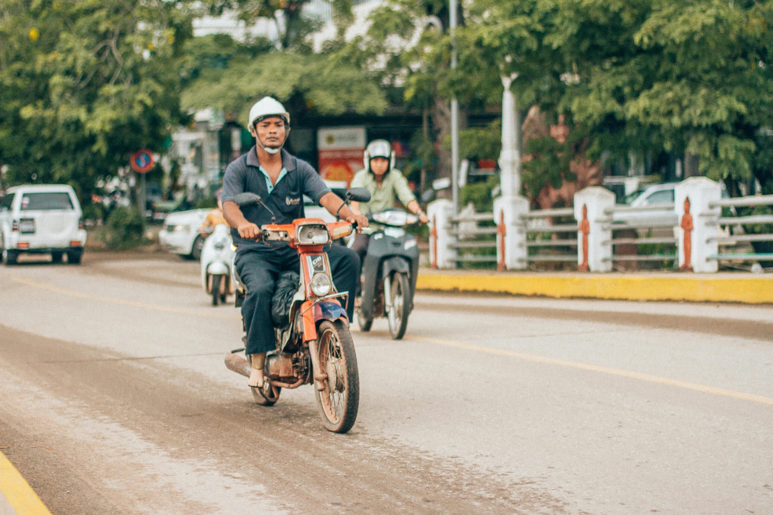 Motorcyclists ride along a bustling street in Siem Reap, Cambodia, showcasing local transportation.