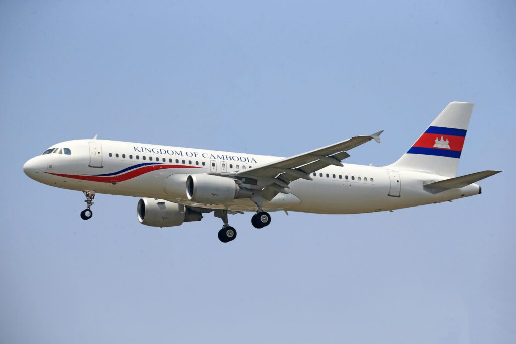 A commercial airplane flying in clear sky with Cambodia's national insignia.