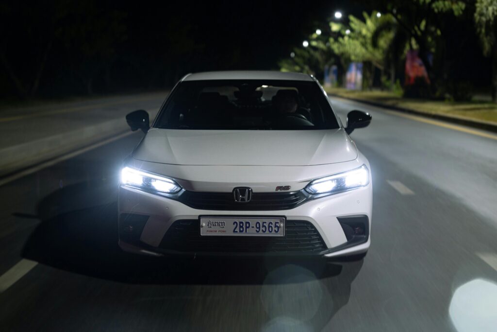 Front view of a white car driving on city streets at night in Phnom Penh, Cambodia.