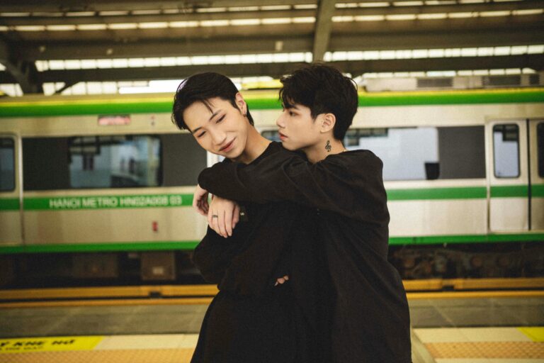 Two men embracing lovingly on a Hanoi Metro platform, capturing urban connection.