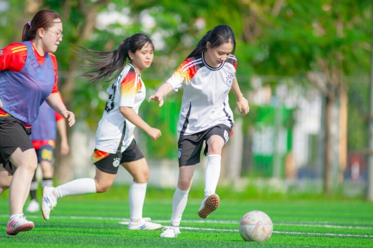 Teenage girls playing soccer outdoors on a sunny day in Hanoi, Vietnam, showcasing teamwork and athleticism.