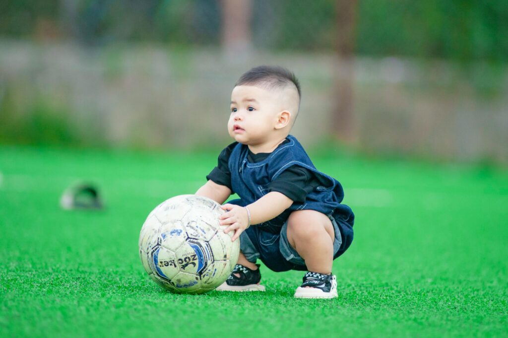 Cute baby playing with a soccer ball on a vibrant green grass field in Hanoi, Vietnam.