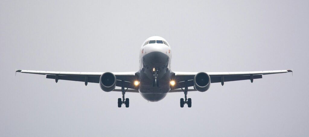 A commercial airliner captured head-on, preparing to land against a cloudy sky.