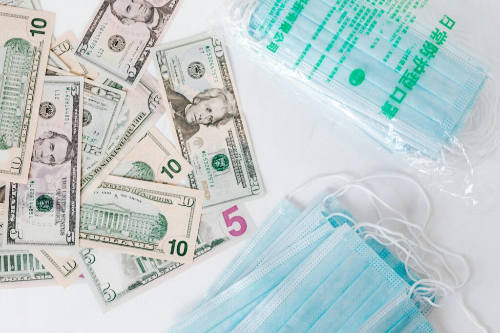 From above composition of stack of USA dollar bills placed near medical protective masks produced in China illustrating concept of medical expenses and deficit during COVID 19