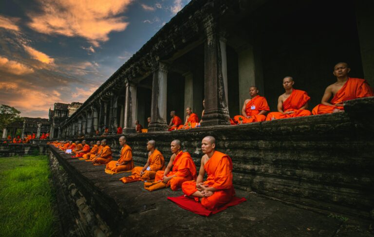 Buddhist monks in orange robes meditate at Angkor Wat, Cambodia during sunset.