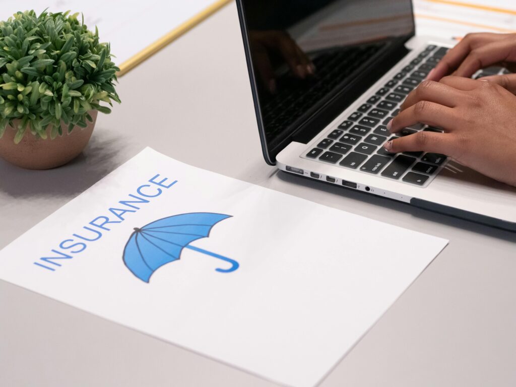 Close-up of hands typing on laptop with an insurance document visible on the desk.