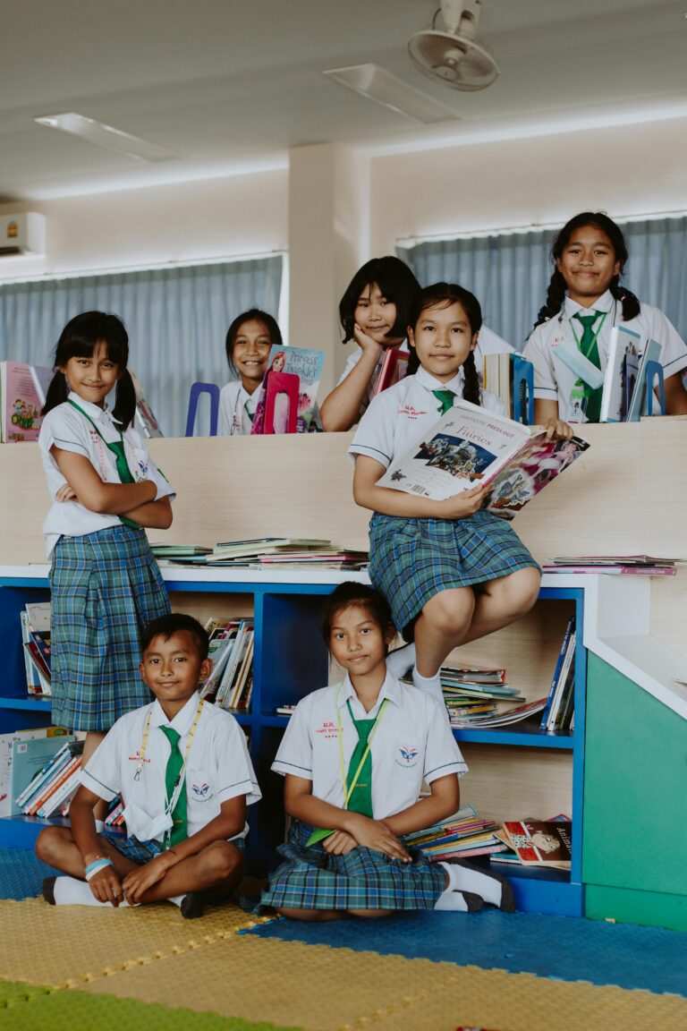 Group of children in school uniforms reading books in a library.