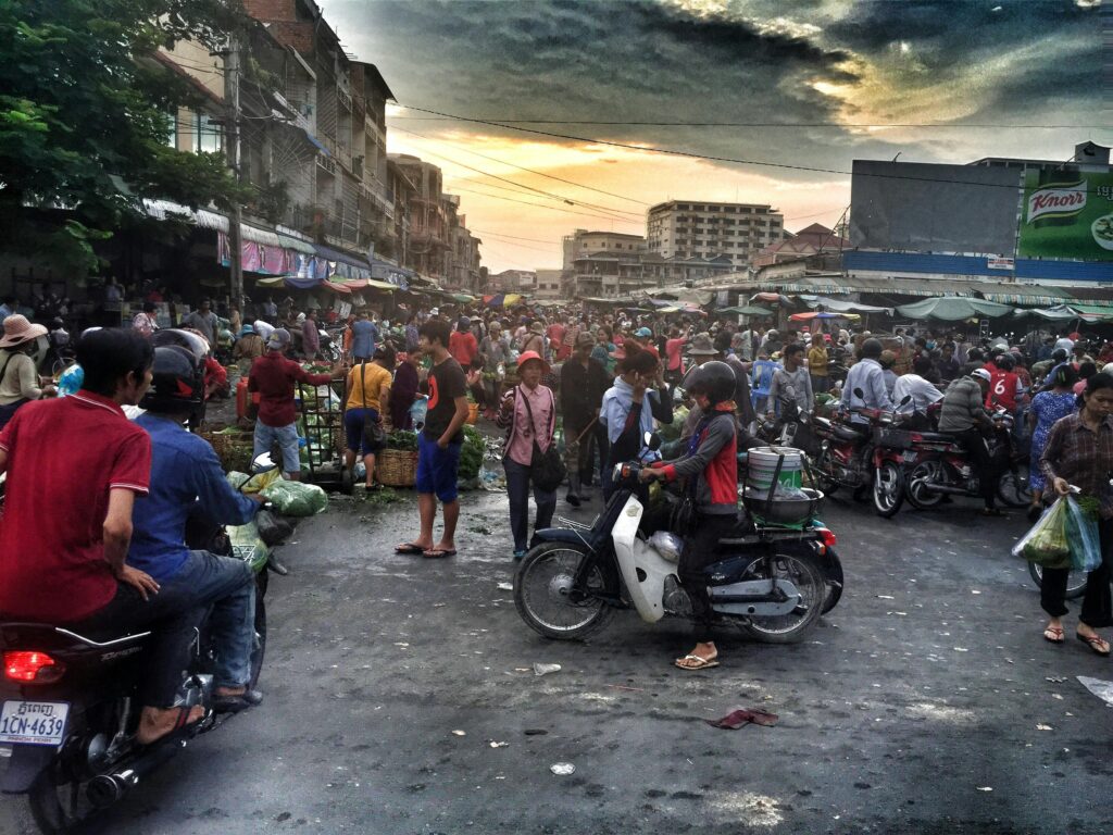 Vibrant street scene in Phnom Penh market filled with people and motorbikes, capturing local life.