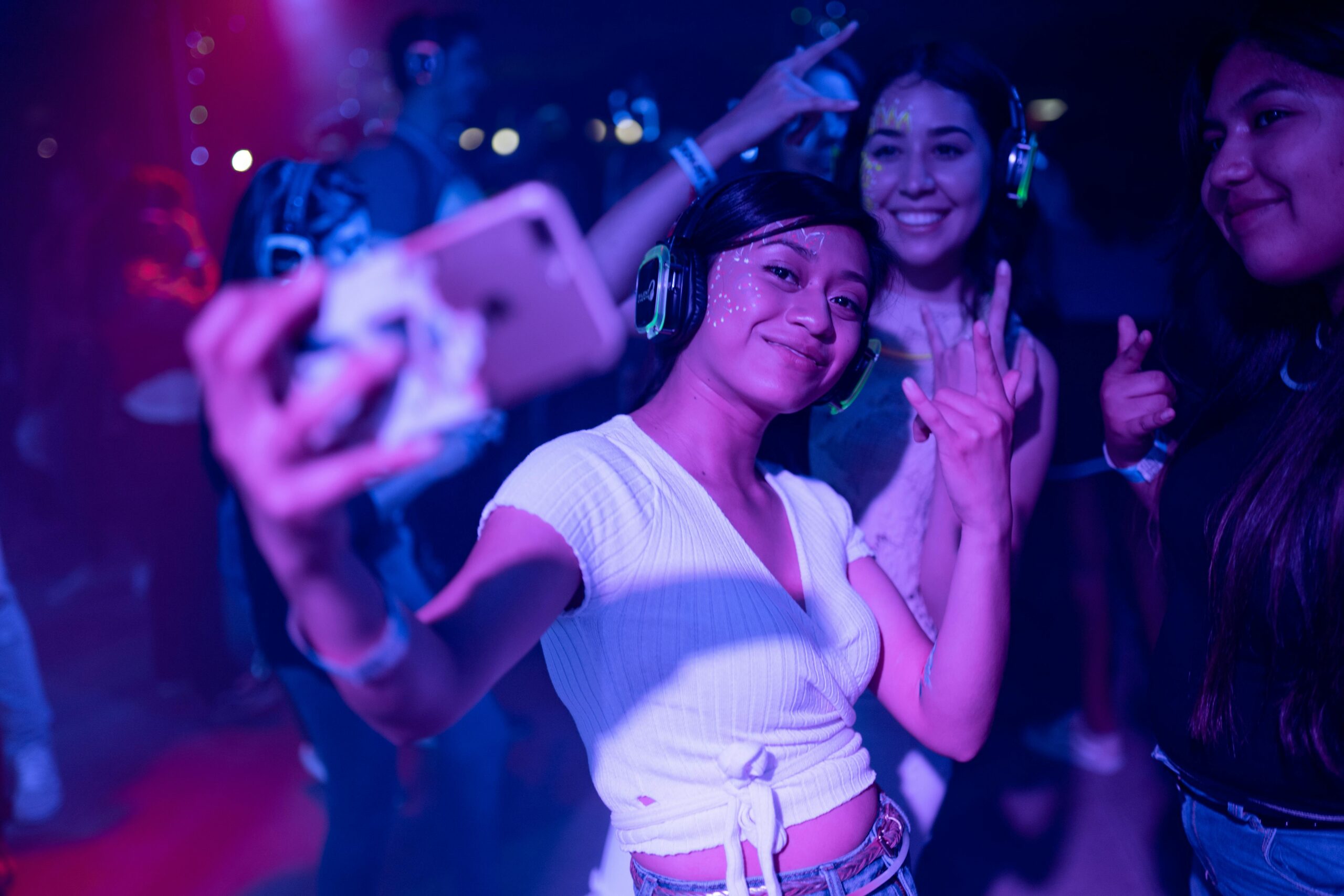 Young adults enjoying a silent disco party, capturing selfies amidst colorful lights.