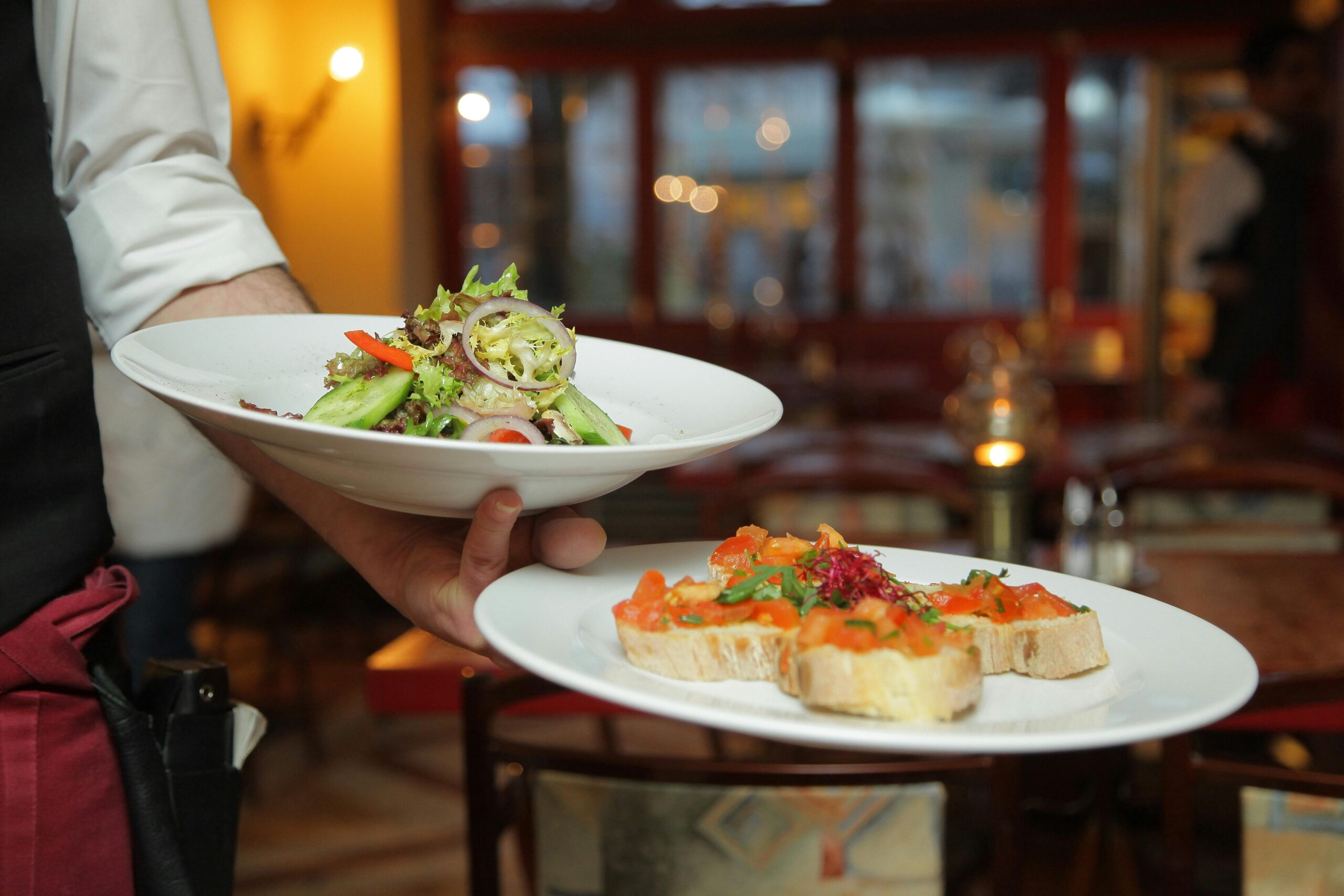 A waiter serves a fresh salad and hors d'oeuvres in a cozy restaurant setting.