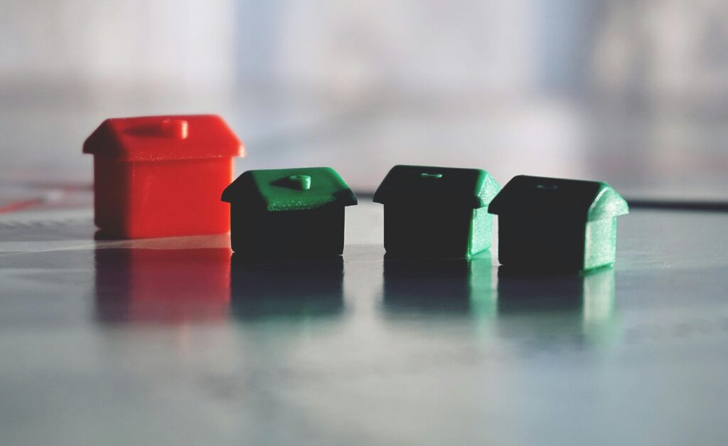 Close-up photo of red and green Monopoly game houses on a reflective surface.