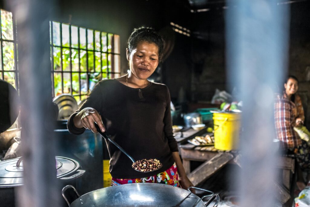 A Cambodian woman cooks with care in a traditional kitchen, showcasing cultural cuisine.