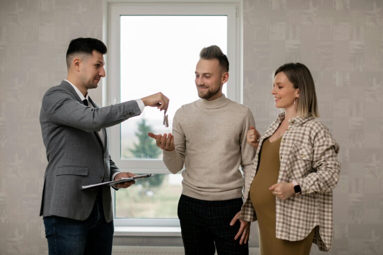 A pregnant woman and her partner receive house keys from a real estate agent indoors.